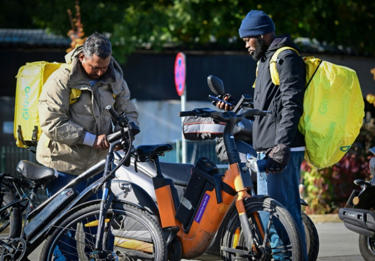 Des livreurs de repas étrangers consultent leurs portables dans une rue de Bucarest, le 10 octobre 2025 en Roumanie ( AFP / Daniel MIHAILESCU )