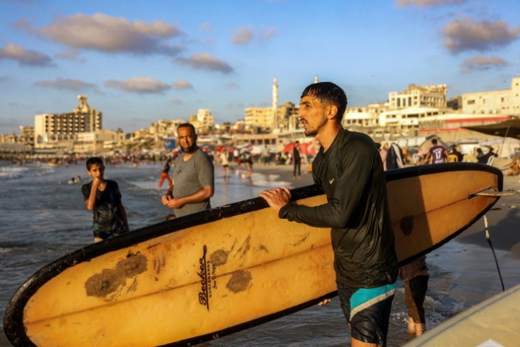 Le Palestinien Tahseen Abu Assi porte sa planche de surf sur une plage de la ville de Gaza, le 21 juin 2026 ( AFP / Omar AL-QATTAA )