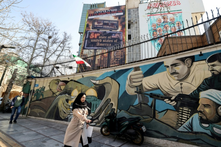 Un passante à Téhéran, devant une affiche hostile à Israël et aux Etats-Unis, le 25 février 2026 ( AFP / ATTA KENARE )
