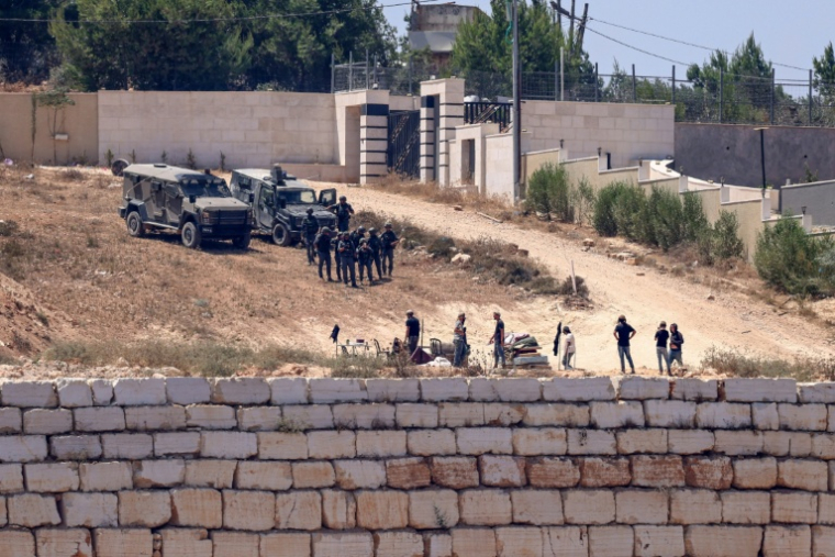 Des soldats israéliens face à des colons assiégeant des maissons palestiniennes du village de Qusra, en Cisjordanie occupée, le 12 août 2026 ( AFP / Zain JAAFAR )