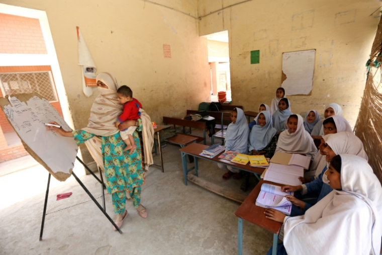 L'enseignante Nazia Hussain (d), son enfant dans les bras, donne un cours dans une école publique du district de Rajanpur, dans la province du sud-ouest du Pendjab, le 15 mai 2025 au Pakistan ( AFP / Shahid Saeed MIRZA )