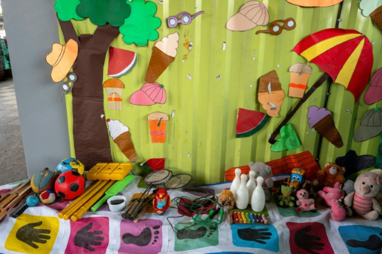 Des peluches et des jeux disposés par terre dans  "l'école du feu rouge", qui accueille des enfants défavorisés dans des conteneurs aménagés en salles de cours sous un pont autoroutier, le 18 mai 2026 à Bombay ( AFP / Punit PARANJPE )