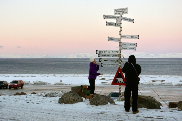 Des touristes chinois prennent des photos devant les célèbres panneaux indicateurs situés à l'aéroport de Longyearbyen, dans l'archipel norvégien du Svalbard, le 18 février 2026 ( AFP / Oriane Laromiguière )