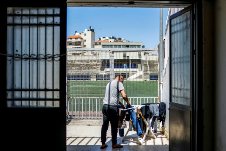 Un Palestinien de Gaza bloqué en Cisjordanie occupée accroche des vêtements sur un étendoir dans un camp installé dans le stade de football de Naplouse, dans le nord de la Cisjordanie occupée, le 7 mai 2026 ( AFP / Zain JAAFAR )