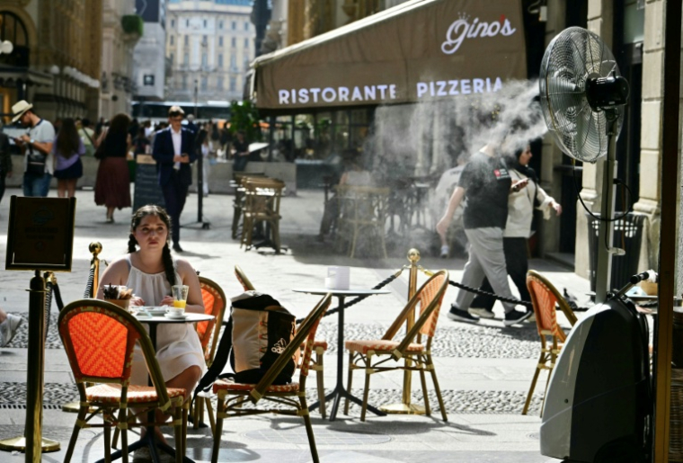 Une jeune fille assise à la terrasse d'un marchand de glaces, sur laquelle un ventilateur-brumisateur a été installé pour se protéger de la chaleur à Milan en Italie, le 27 mai 2026 ( AFP / Stefano RELLANDINI )