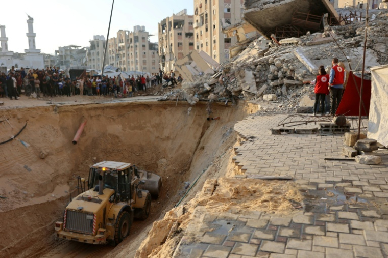 Des habitants et des membres de la Croix rouge regardent un tractopelle creuser, selon les autorités locales pour chercher les corps des otages, le 17 octobre 2025 à Khan Yunes ( AFP / Omar AL-QATTAA )