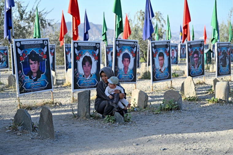 Une femme afghane et un enfant assis dans un cimetière des membres de la communauté hazara, à Tapa-e-Shuhada (la colline des Martyrs), Kaboul, le 25 août 2026 ( AFP / Wakil KOHSAR )