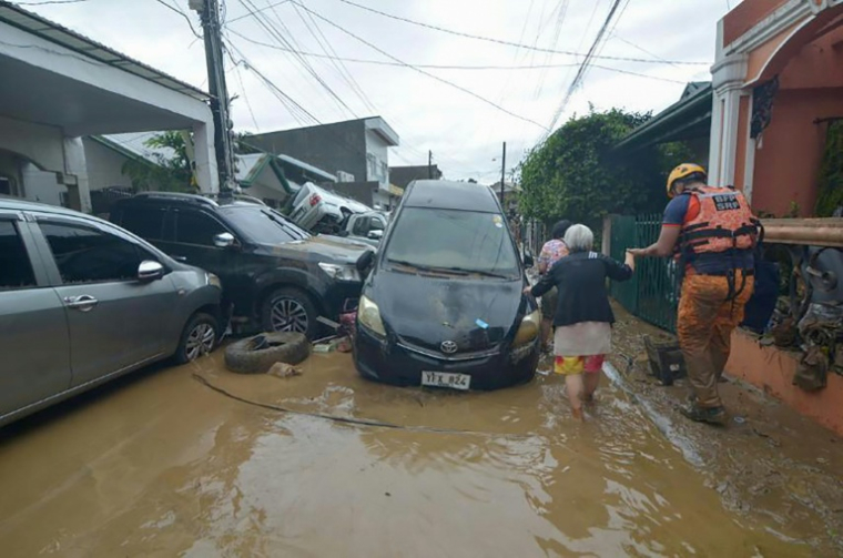 Un sauveteur aide un habitant à passer devant des voitures emportées par les inondations au plus fort du typhon Kalmaegi dans un quartier de la ville de Cebu, dans le centre des Philippines, le 4 novembre 2025 ( AFP / Alan TANGCAWAN )