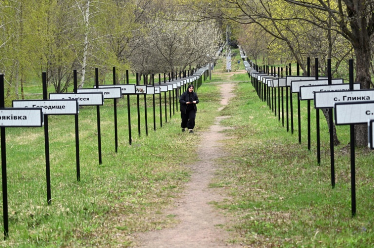 Une femme marche le 23 avril 2026 dans la ville de Tchernobyl, le long de l'allée commémorative portant les noms des villages disparus de la région ( AFP / Sergei SUPINSKY )