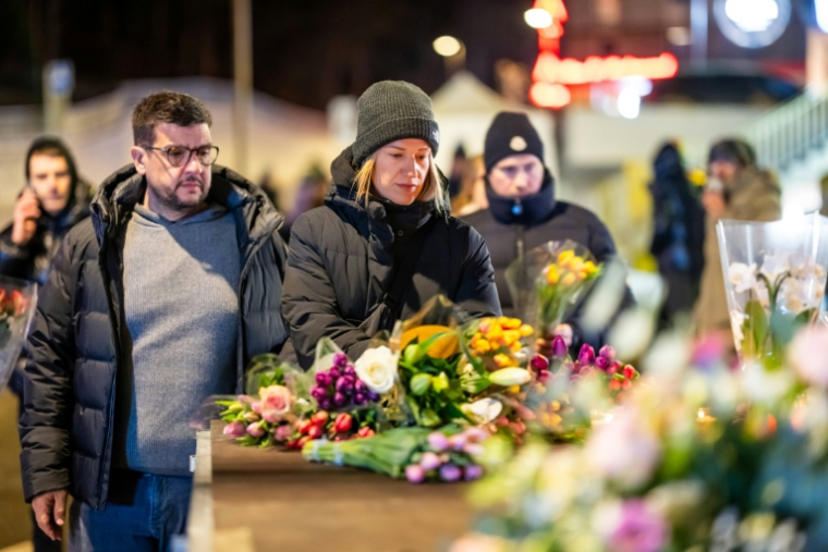 Des personnes en deuil se rassemblent devant des fleurs et des bougies déposées près du lieu où un incendie a ravagé un bar bondé lors des célébrations du nouvel an dans la station de ski alpine de Crans-Montana, le 1er janvier 2026  ( AFP / MAXIME SCHMID )