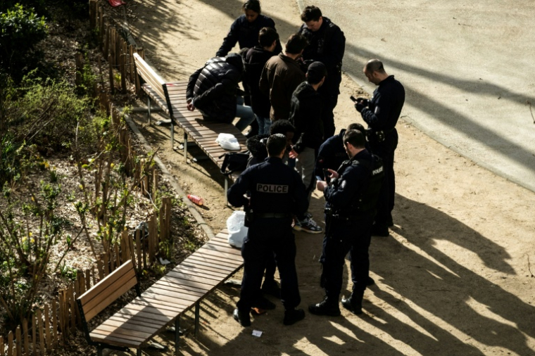 Des policiers contrôlent des migrants présumés dans un square place de La Chapelle à Paris, le 12 mars 2020 ( AFP / JOEL SAGET )