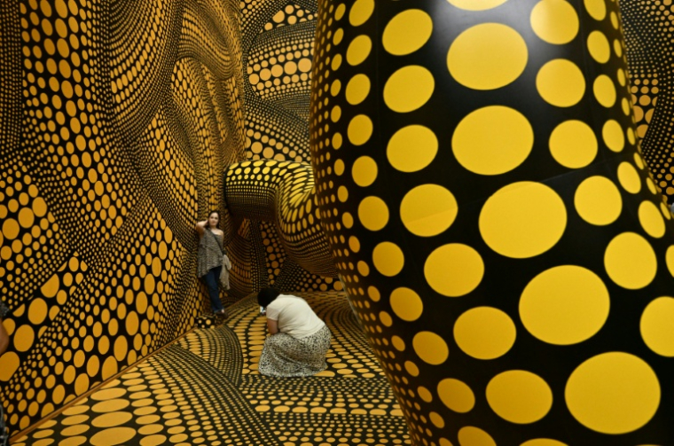 Des visiteurs prennent des photos tandis qu’ils dans l’installation "Infinity Mirrored Room – The Hope of the Polka Dots Buried in Infinity Will Eternally Cover the Universe" lors du dernier jour de l’exposition "Yayoi Kusama" de l’artiste japonaise au musée Ludwig à Cologne, en Allemagne, le 2 août 2026 ( AFP / Ina FASSBENDER )