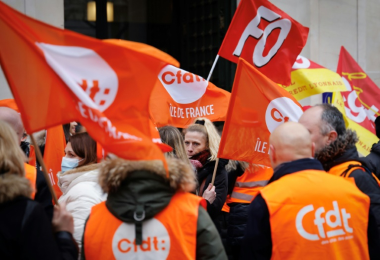Des grévistes brandissent des drapeaux des syndicats CFDT, CGT et FO, le 17 janvier 2023 à Paris ( AFP / Ludovic MARIN )