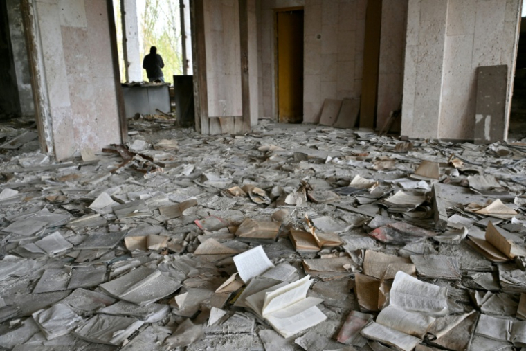 Un visiteur marche parmi des livres jonchant le sol du Palais de la culture, abandonné, dans la ville fantôme de Pripyat, près de la centrale nucléaire de Tchernobyl, le 23 avril 2026 ( AFP / Sergei SUPINSKY )