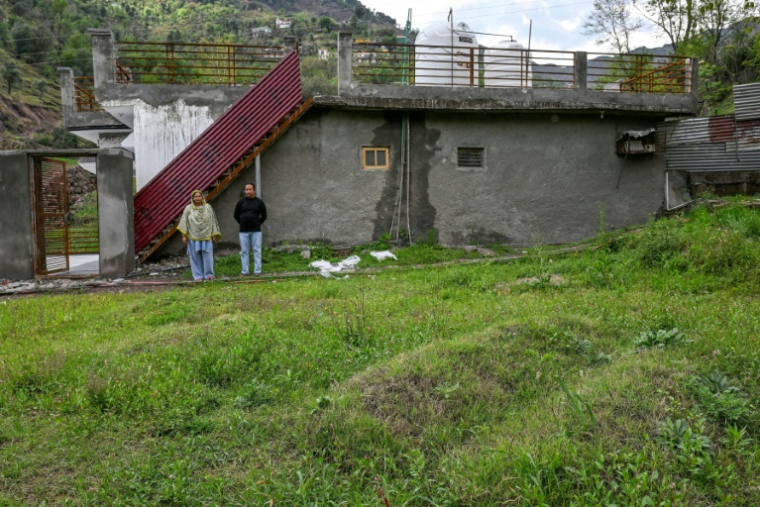 Rameez Khan (d) et son épouse Urusa Khan, qui ont perdu leurs jumeaux en fuyant lors du conflit indo-pakistanais de 2025, se tiennent près de leurs tombes devant leur maison dans le district frontalier de Poonch, le 6 avril 2026 en Inde ( AFP / Tauseef MUSTAFA )