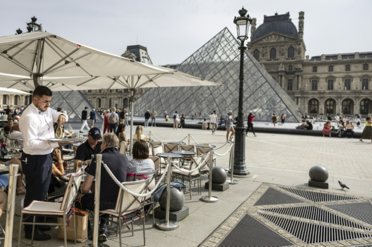 Un serveur sur une terrasse de restaurant près de la Pyramide du Louvre, conçue par l'architecte sino-américain Ieoh Ming Pei, au musée du Louvre, l'un des lieux qui sera rafraîchi avec l'eau de la Seine ( AFP / Olympia DE MAISMONT )