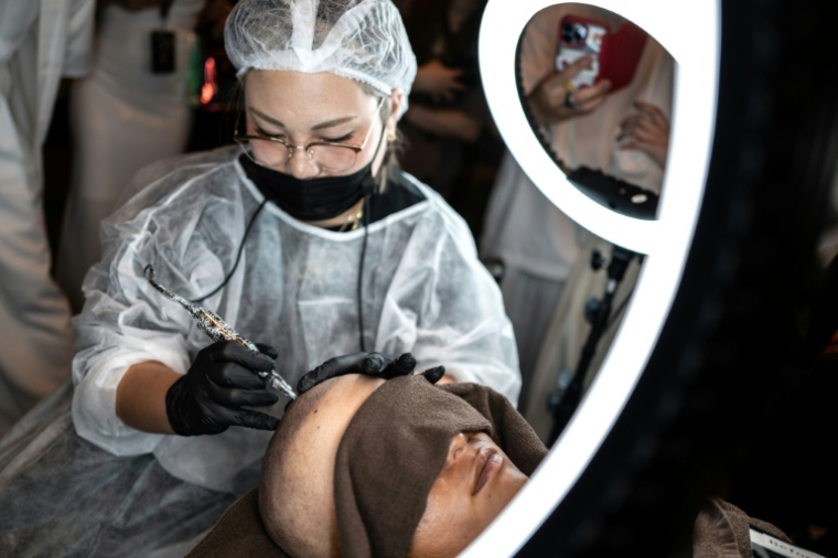 Un tatoueur spécialisé dans le tatouage du cuir chevelu lors d'un concours à Naha, dans la préfecture d'Okinawa, au Japon, le 8 juillet 2026 ( AFP / Philip FONG )