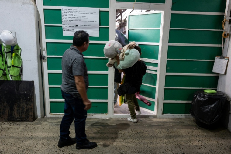 Jose Maria Garcia (g), directeur du refuge Juventud 2000, observe une mère et son fils quittant le refuge à Tijuana, dans l’État de Basse-Californie, le 19 octobre 2026 au Mexique ( AFP / Guillermo Arias )