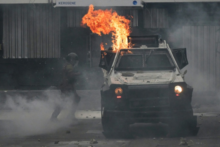Un policier antiémeute près d'un véhicule incendié à Santiago durant des affrontements entre policiers et manifestants qui participaient le 7 septembre à la marche annuelle en hommage aux victimes de la dictature instaurée au Chili par Augusto Pinochet ( AFP / RODRIGO ARANGUA )