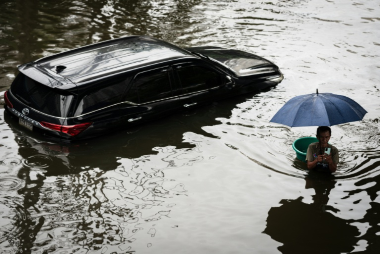 Un homme passe devant uen voiture sous les eaux à Bangkok, où l'état de catastrophe naturelle a été déclaré après des pluies diluviennes qui ont inondé habitations, commerces et axes de circulation, le 27 septembre 2026 ( AFP / Chanakarn LAOSARAKHAM )