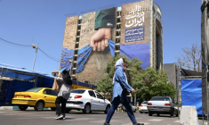 Des passants près d'un panneau d'affichage sur la façade d'un immeuble représentant le détroit d'Ormuz avec une inscription en persan disant "À jamais dans la main de l'Iran", place Vanak à Téhéran, le 25 mai 2026 ( AFP / ATTA KENARE )