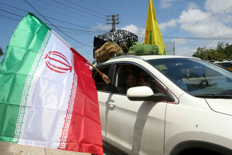 Une femme déplacée tient un drapeau iranien à la fenêtre d'une voiture, alors qu'elle traverse la région d'al-Qasmiyeh, dans le sud du Liban, sur le chemin du retour vers son village natal, le 15 juin 2026  ( AFP / Mahmoud ZAYYAT )