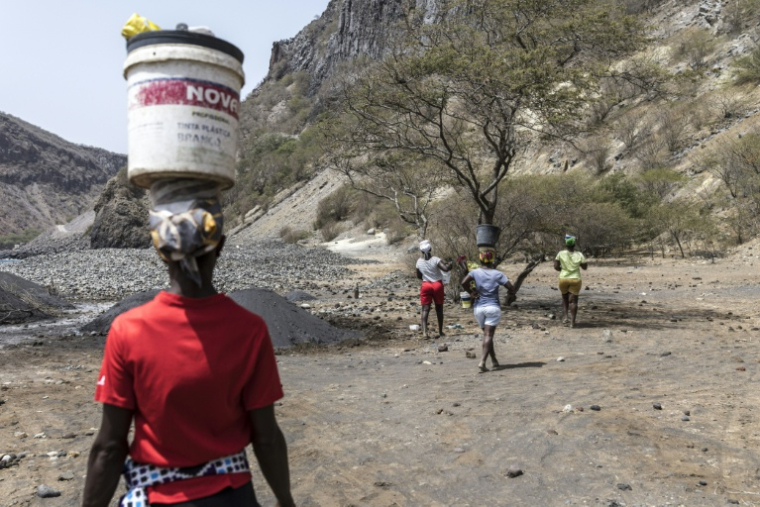 Des femmes portent des seaux en équilibre sur leur tête après avoir ramassé du sable noir destiné à la vente, près de Ribeira da Barca, le 20 mai 2026 au Cap-Vert ( AFP / PATRICK MEINHARDT )