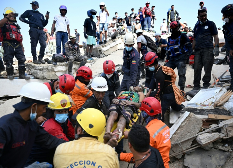 Des membres de la protection civile vénézuélienne et des pompiers sortent un jeune homme des décombres d'un immeuble effondré à Catia La Mar, dans l'Etat de La Guaira, au Venezuela, le 26 juin 2026 ( AFP / Federico PARRA )
