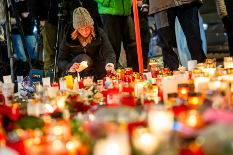 Une femme allume une bougie devant un mémorial improvisé près du lieu de l'incendie qui a ravagé un bar lors des célébrations du nouvel an dans la station de ski alpine de Crans-Montana, le 2 janvier 2026 ( AFP / MAXIME SCHMID )