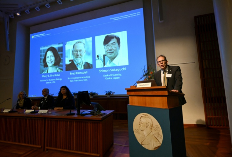 Le secrétaire général du comité Nobel Thomas Perlmann (d) près des portraits de Mary E. Brunkow, Fred Ramsdell et Shimon Sakaguchi, lauréats du Nobel de médecine, à Stockholm le 6 octobre 2025 ( AFP / Jonathan Nackstrand )