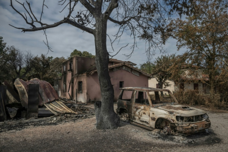 Une voiture calcinée devant une maison détruite par l'incendie, au Porge, dans le sud-ouest de la France, le 31 juillet 2026 ( AFP / Ed JONES )