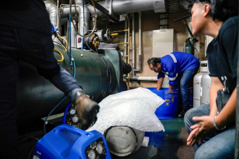 Des techniciens de la société Recoolit travaillent à capturer les gaz de refroidissemen d'une grande unité de climatisation au sous-sol d'un complexe d'habitation à Jakarta, le 10 juin 2025 en Indonésie ( AFP / Jack Moore )