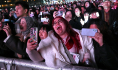 Des fans de BTS assistent au concert de retour du boys band de K-pop devant un écran installé sur le lieu de l'événement à Séoul, le 21 mars 2026 ( AFP / Jung Yeon-je )