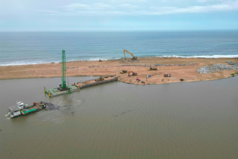 Vue aérienne montrant les travaux de construction d'une nouvelle embouchure, à Lahou-Kpanda, village situé à 140 km d'Abidjan (Côte d'Ivoire), entre mer et lagune, et menacé par l'érosion, le 3 août 2025 ( AFP / Issouf SANOGO )