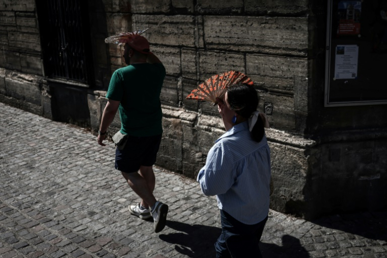 Des passants se protègent du soleil, le 1er juillet 2025 à Paris en période de canicule ( AFP / Thibaud MORITZ )