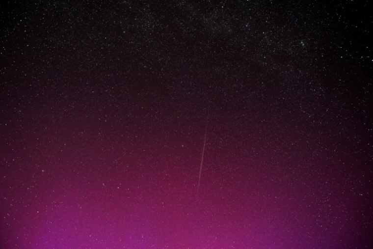 Une photo en pose longue montre une traînée laissée par un groupe de satellites Starlink de SpaceX, dans un ciel illuminé par des aurores boréales  pendant la pluie annuelle d'étoiles filantes des Perséides, le 12 août 2024 à Wigry, en Pologne ( AFP / Sergei GAPON )