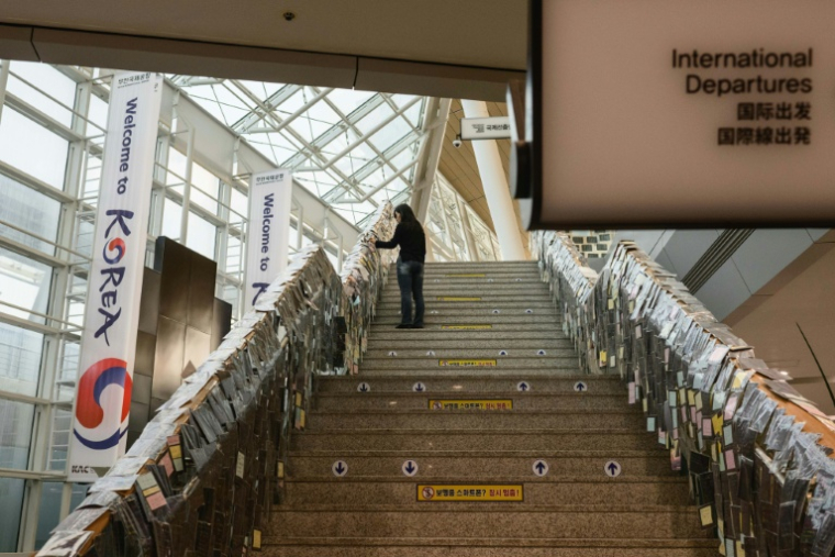 Lee Hyo-eun regarde les messages laissés à la mémoire des victimes du crash du vol 2216 de Jeju Air en décembre 2024, dans le hall des départs de l'aéroport international de Muan, le 14 décembre 2025 en Corée du Sud ( AFP / ANTHONY WALLACE )
