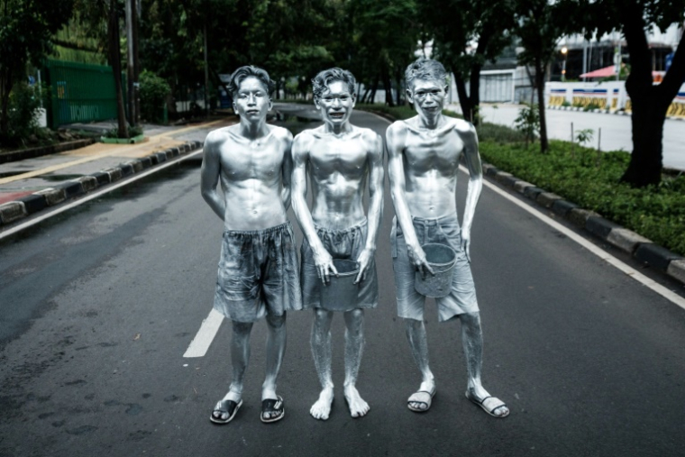Les artistes de rue Keris Munandar (d), son frère Ari Munandar (c) et leur voisin Riyan Ahmad Fazriyansah dans une rue de Jakarta, le 1er avril 2025 en Indonésie ( AFP / Yasuyoshi CHIBA )