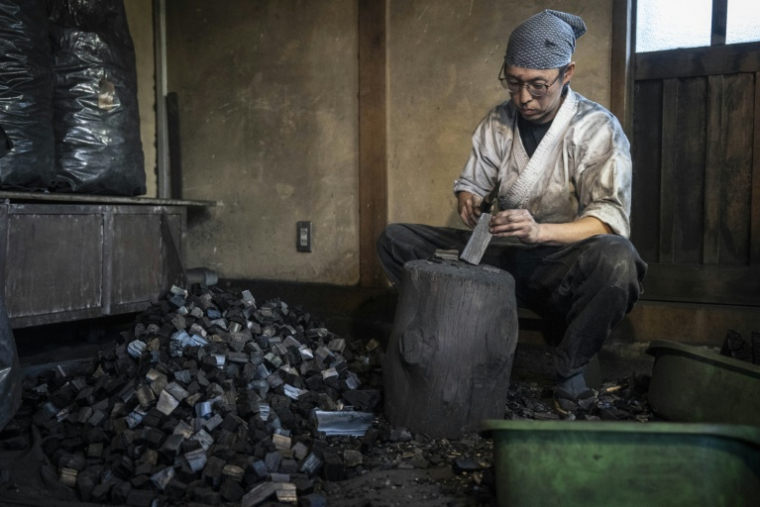Toru Watanabe, apprenti du forgeron Akihira Kawasaki, casse du charbon de bois dans l'atelier de Kawasaki à Misato, le 9 janvier 2026 au Japon ( AFP / Yuichi YAMAZAKI )