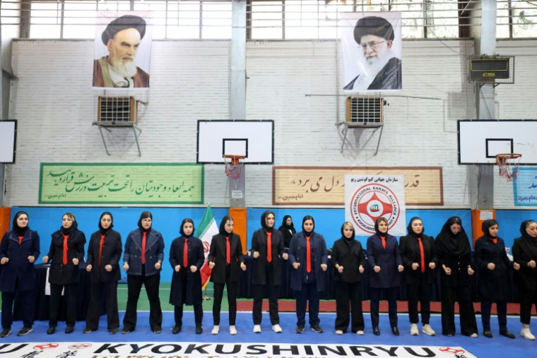 Des femmes se mettent en rang d'oignon avant le début d'une compétition de karaté à Téhéran le 6 novembre 2025, sous les portraits de l'imam Khomeini, fondateur de la République islamique, et son successeur au pouvoir depuis 1989. ( AFP / ATTA KENARE )