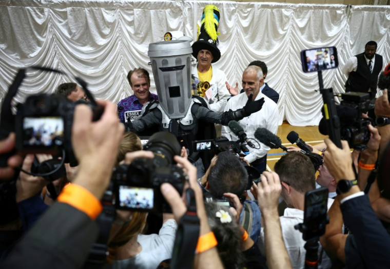 Le comte Tête-de-Poubelle (C) pose avec les autres candidats après la proclamation des résultats de l'élection partielle de Clacton au Clacton Leisure Centre, dans l'est de l'Angleterre, le 14 août 2026 ( AFP / Henry NICHOLLS )