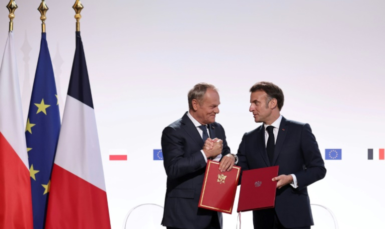 Le Premier ministre polonais Donald Tusk (g) et le président français Emmanuel Macron se serrent la main après avoir signé un traité à l'issue de leur rencontre à Nancy, le 9 mai 2025 ( POOL / Christophe PETIT TESSON )