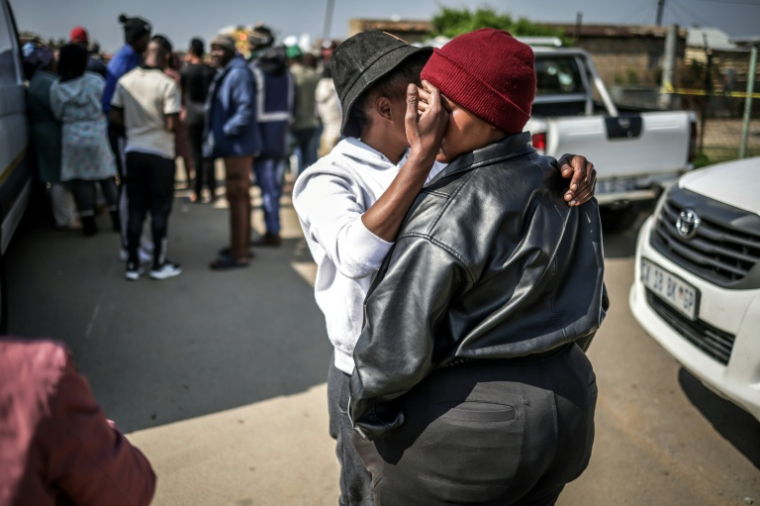 Un résident réconforte une autre personne près du lieu où des hommes armés de fusils d’assaut ont tué 17 personnnes dans un bar à Johannesburg le 27 septembre 2026 ( AFP / EMMANUEL CROSET )