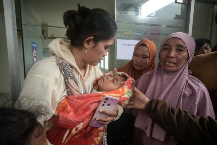 Une femme porte un enfant qui a surcévu à un glissement de terrain dans le village de Pasirlangu, dans la région du Bandung occidental, au sud-est de Jakarta, le 24 janvier 2026 ( AFP / Timur Matahari )
