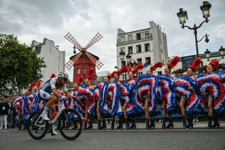 Le Français Valentin Madouas passe devant les danseuses du cabaret du Moulin Rouge à Montmartre lors de la course en ligne hommes des Jeux olympiques de Paris le 3 août 2024 ( AFP / Mauro PIMENTEL )