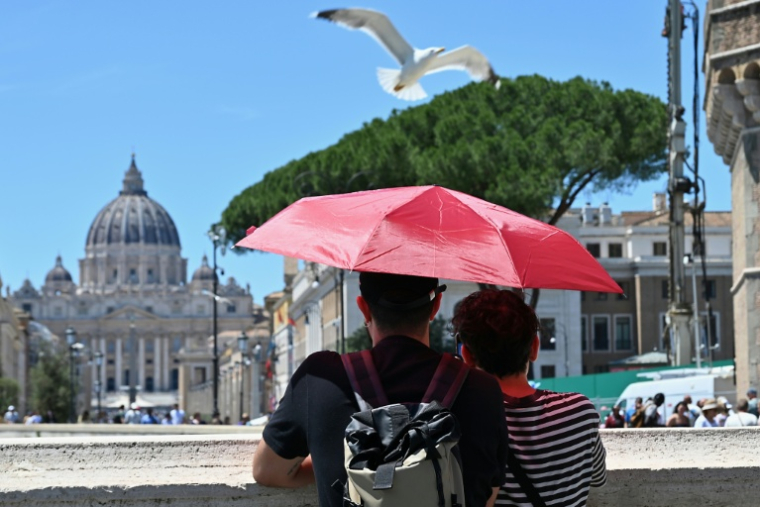 Un couple se protège du soleil avec un parapluie en admirant le Vatican depuis le pont Sant'Angelo à Rome, le 23 mai 2026 en Italie ( AFP / ANDREAS SOLARO )