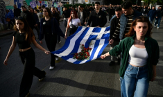 Des participants au défilé de commémoration du soulèvement étudiant de 1973 contre la junte en Grèce portent un drapeau grec sur lequel sont posés des oeillets rouges, à Athènes le 17 novembre 2025 ( AFP / Aggelos NAKKAS )