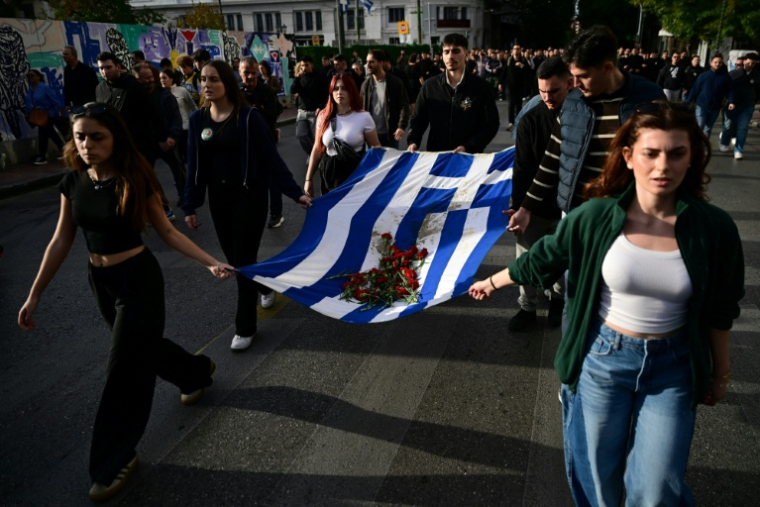 Des participants au défilé de commémoration du soulèvement étudiant de 1973 contre la junte en Grèce portent un drapeau grec sur lequel sont posés des oeillets rouges, à Athènes le 17 novembre 2025 ( AFP / Aggelos NAKKAS )