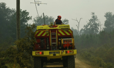 Un camion pompier survolé par un appui aérien le 15 août 2026 dans la forêt des Landes en flammes près de Luglon ( AFP / Gaizka IROZ )