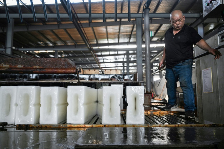 Un ouvrier transporte des blocs de glace vers un camion réfrigéré à l'usine de production de glace Feichao à Hangzhou, dans la province orientale du Zhejiang, le 9 juillet 2025 en Chine ( AFP / Hector RETAMAL )